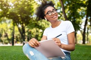 teen writing in notebook in a park